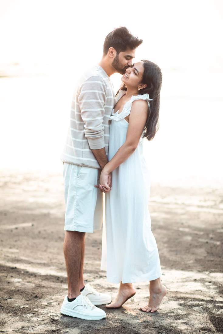 Groom kissing bride's forehead, both laughing, on the beach