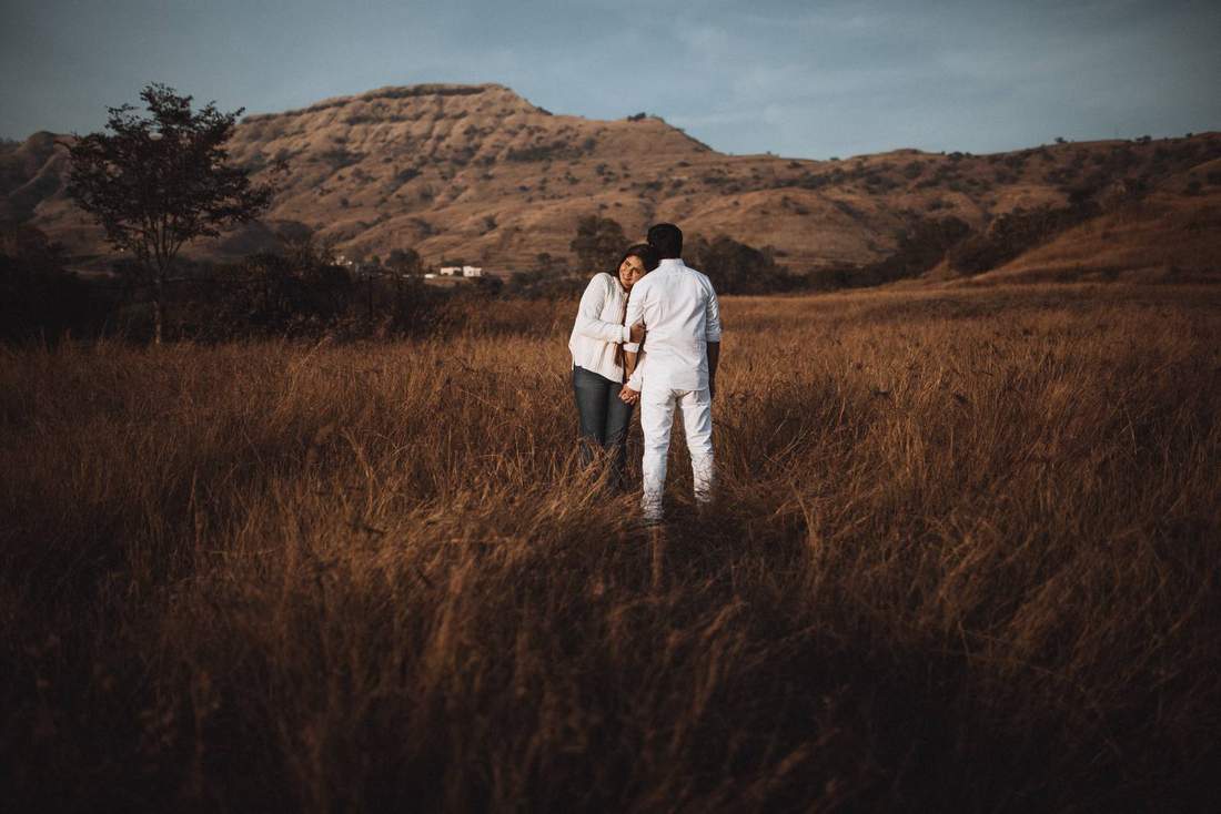 Couple walking through golden grassland with hills behind them