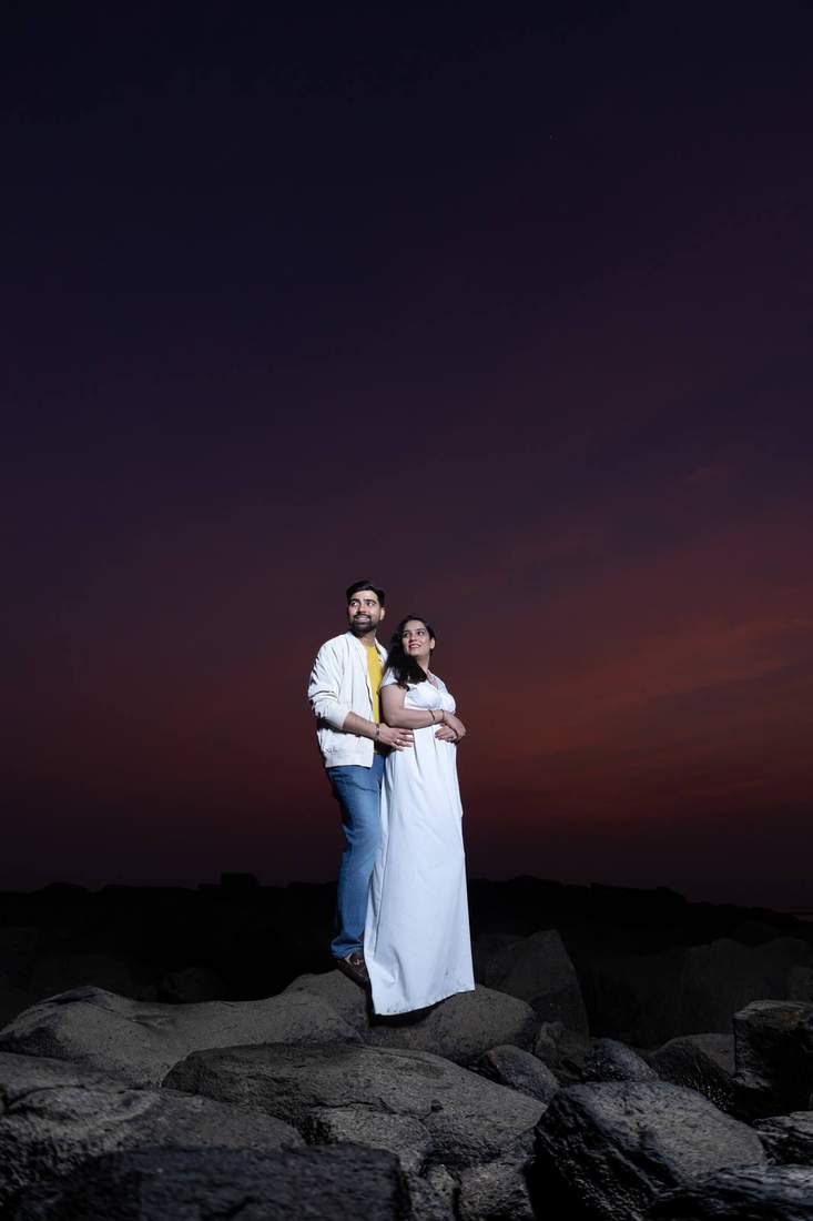 Couple posed together on rocks under a dusk sky