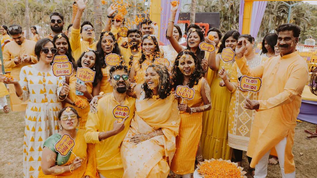 Bride and groom surrounded by friends holding playful haldi signs