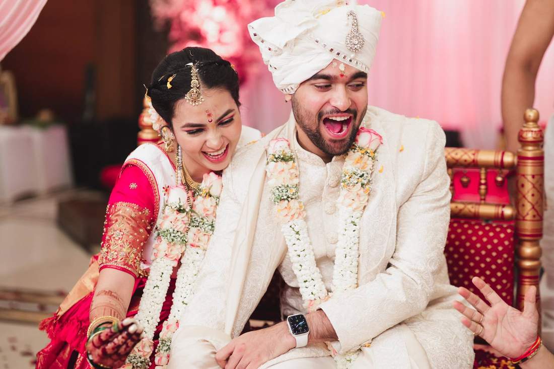 Bride and groom laughing together, close, wearing floral garlands