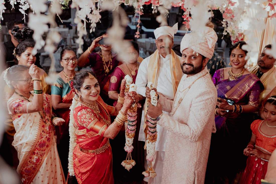 Bride and groom exchanging garlands as family looks on