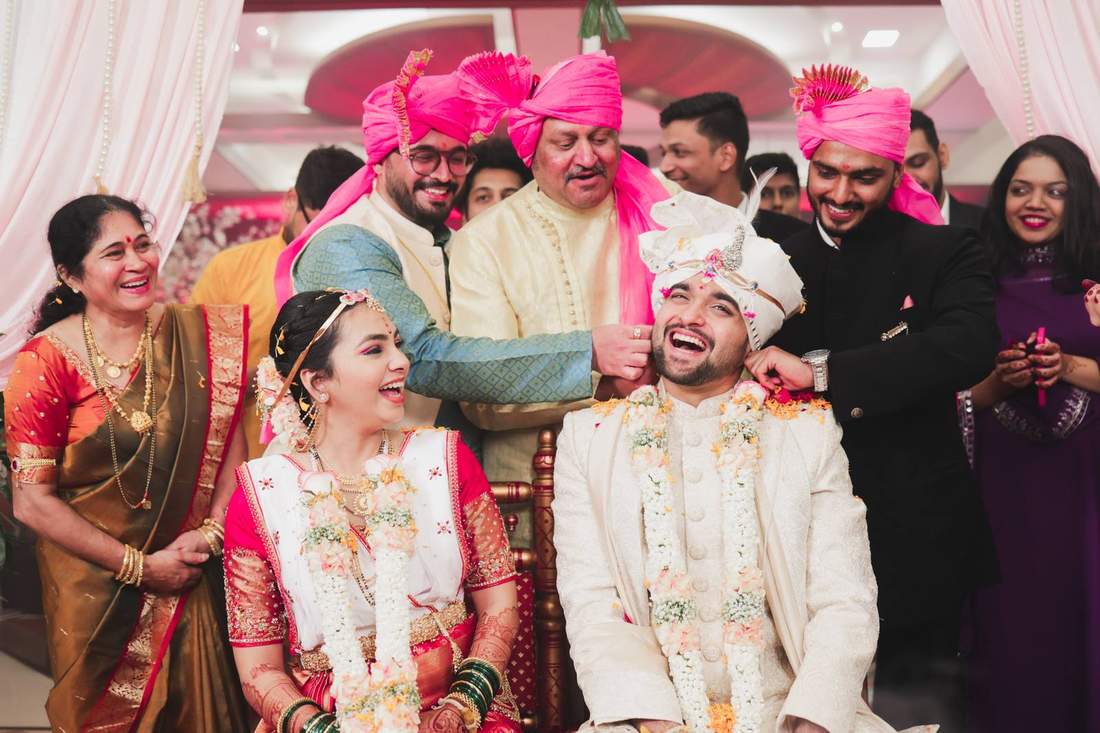 Family placing a garland on the groom as the bride laughs beside him