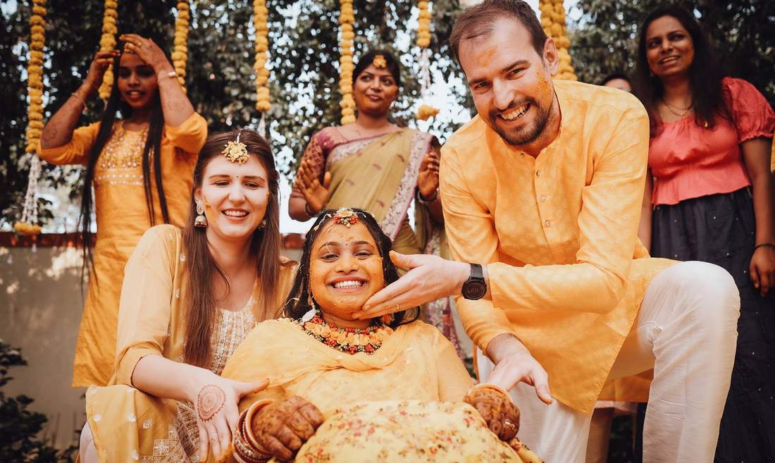 Bride laughing, covered in turmeric, surrounded by family during haldi