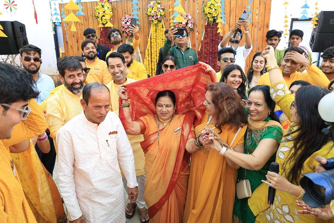 Family blessing moment, an elder held under a red dupatta by loved ones
