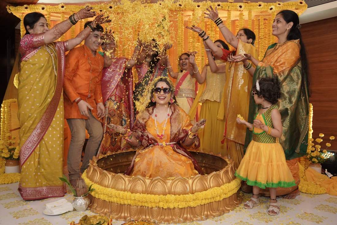 Bride seated in a golden lotus-shaped tub as family showers her with petals