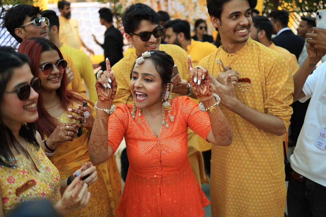 Friends dancing together, hands raised, at the sangeet